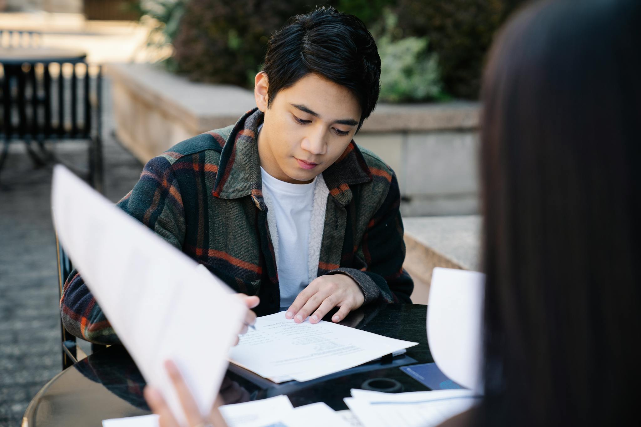 A focused young Asian man studying at an outdoor table, preparing for exams.