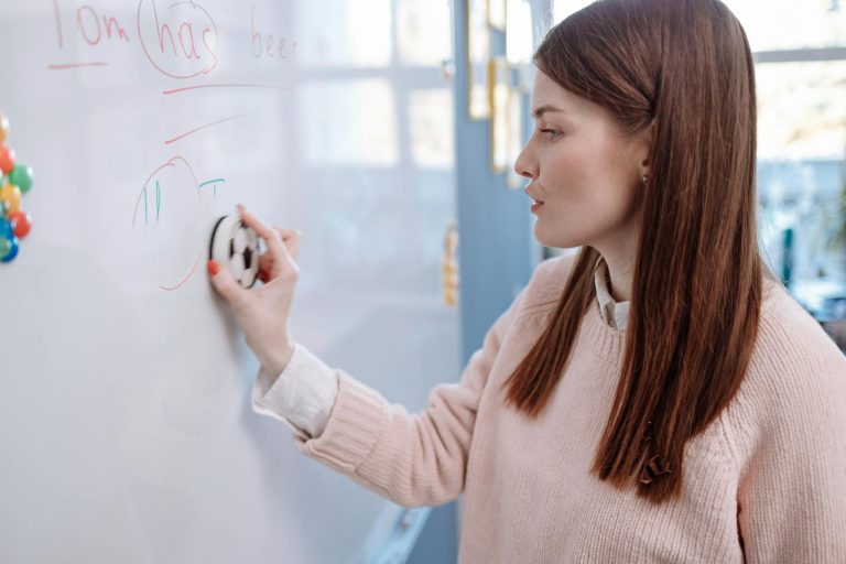 A woman teacher erasing writing on a whiteboard in a classroom setting.