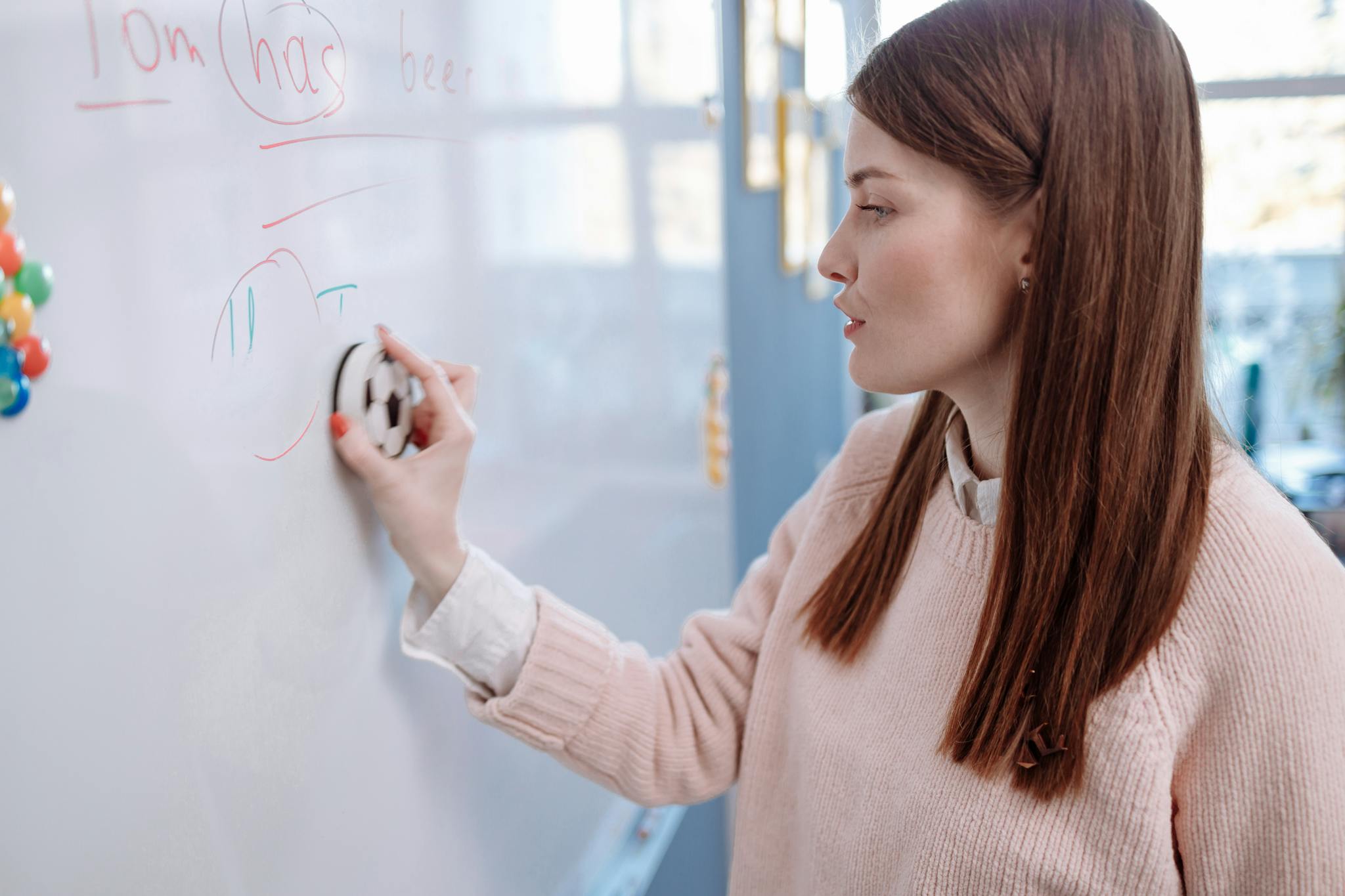 A woman teacher erasing writing on a whiteboard in a classroom setting.