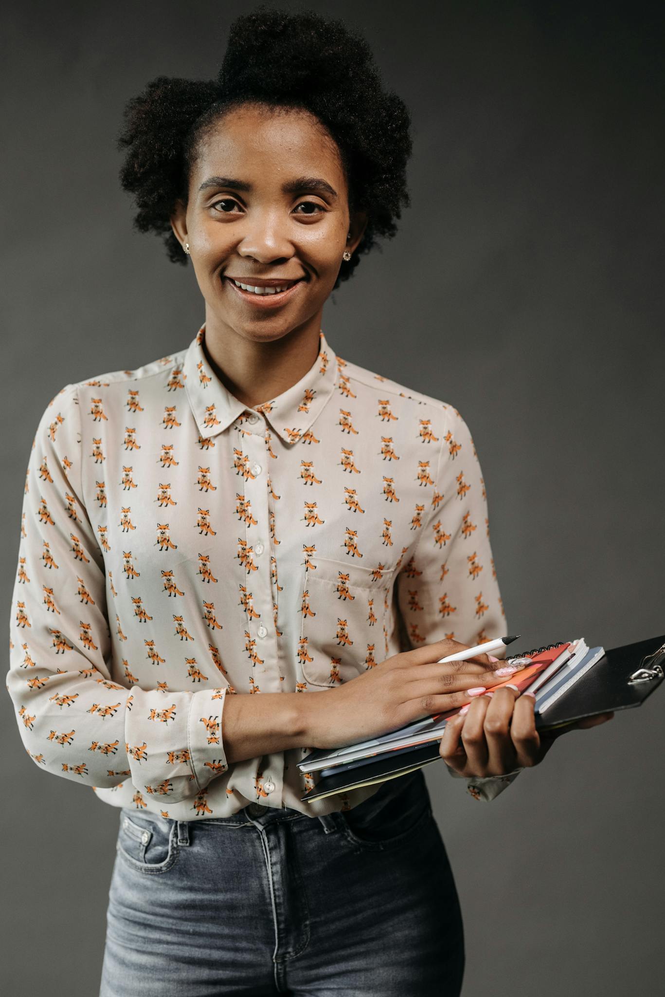 Portrait of a smiling female teacher with afro hair holding books in a studio setting.
